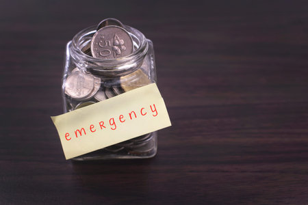 Finacial concept. Money in the glass on wooden table with emergency word and copy space area.の写真素材