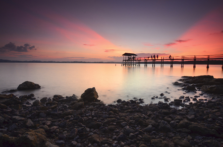 Beautiful sunset over wooden jetty with silhoutte of man fishing.の写真素材