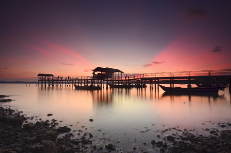 Beautiful sunset over wooden jetty with silhoutte of man fishing.の写真素材