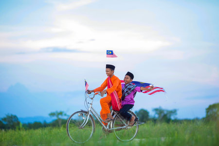 Two happy young local boy riding old bicycle at paddy field with Malaysian flag - Indepence Day...