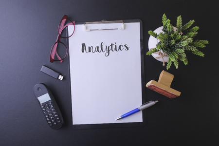 Notebook writing "Analytics" on table, Working space at the office with cell phone ,usb drive,glasses and green plantの写真素材