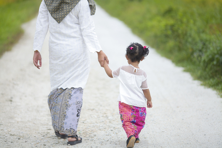 Mom holding her baby girl hand with hari raya dress.の写真素材