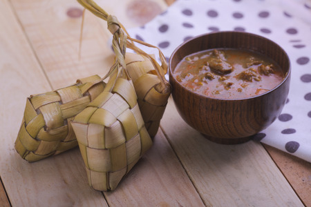 Ketupat (Rice Dumpling) and curry On wooden Background. Ketupat is a natural rice casing made from young coconut leaves for cooking rice during eid Mubarakの写真素材