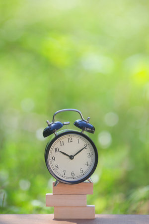 Black alarm clock stacked on wooden bar with shallow DOF green background. Business / Time...