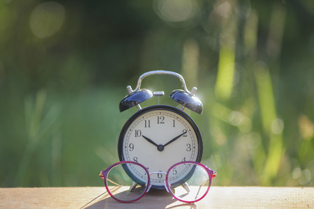 Black alarm clock stacked on wooden bar with purple glasses green backgroundの写真素材