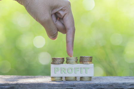 Finger pointing to profit word, golden coin stacked on green nature background. Business concept.の写真素材