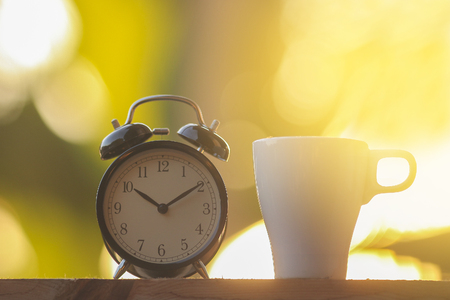 Black alarm clock and a cup of coffee with dramatic morning lightの写真素材