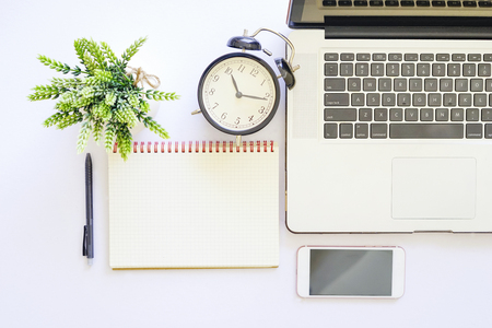 Flat lay top view of white table with notebook, a pen, smartphone and green plantの写真素材