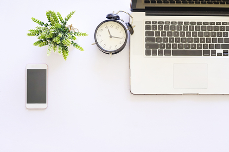 Flat lay top view of white table with notebook, a pen, smartphone and green plantの写真素材
