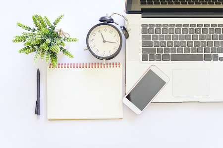 Flat lay top view of white table with notebook, a pen, smartphone and green plantの写真素材
