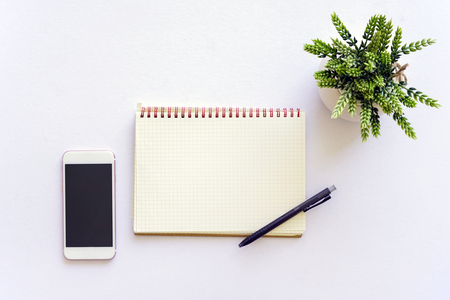 Flat lay top view of white table with notebook, a pen, smartphone and green plantの写真素材