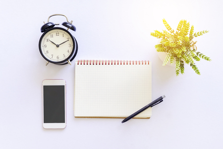 Flat lay top view of white table with notebook, a pen, smartphone and green plantの写真素材