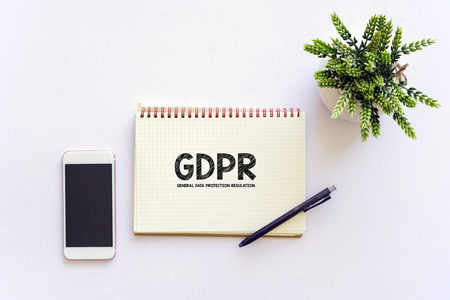 Flat lay top view of white table with notebook, a pen, smartphone and green plant, GDPR WORDの写真素材