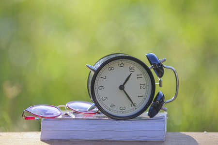 Black alarm clock stacked on old dictionary with pink flower and glasses.の写真素材