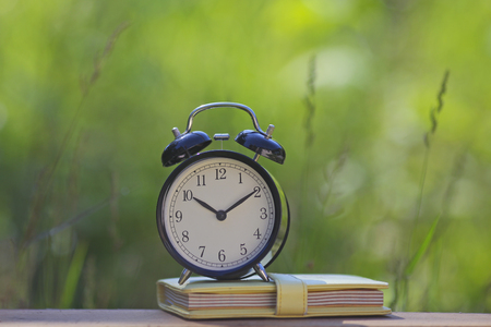 Black alarm clock stacked on organize book with nature bokehの写真素材