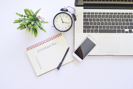 Top view of office table with black alarm clock, laptop and notepad written 2019 Action Planの写真素材