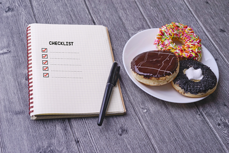 Checklist concept - checklist box with red checkmark, paper, doughtnut and a pen with checklist word on wooden tableの写真素材
