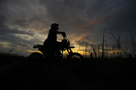 Silhouette of a man riding his motorcycle during sunsetの写真素材