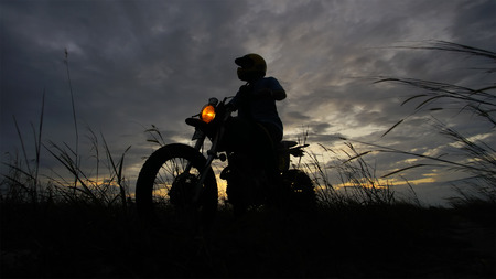 Silhouette of a man riding his motorcycle during sunsetの写真素材