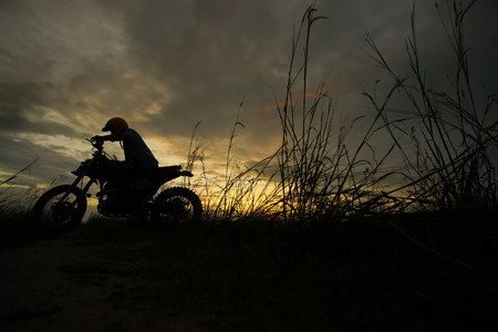 Silhouette of a man riding his motorcycle during sunsetの写真素材