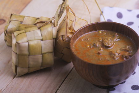 Ketupat (Rice Dumpling) and curry On wooden Background. Ketupat is a natural rice casing made from young coconut leaves for cooking rice during eid Mubarakの写真素材