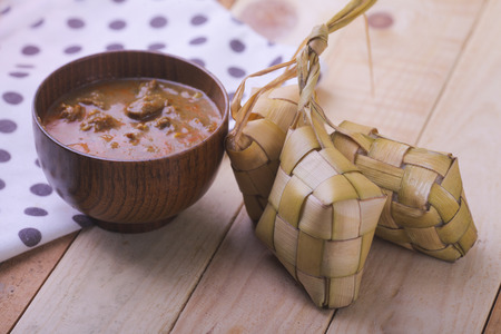 Ketupat (Rice Dumpling) and curry On wooden Background. Ketupat is a natural rice casing made from young coconut leaves for cooking rice during eid Mubarakの写真素材