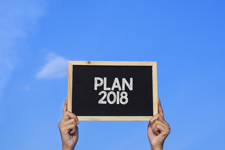 PLAN 2018 / Man holding small blackboard on blue skyの写真素材