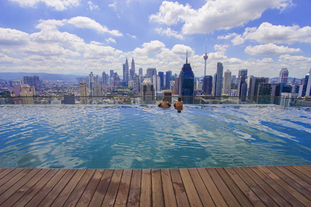 Unidentified businessman and traveller swimming in infinity pool with Kuala Lumpur City skylineの写真素材