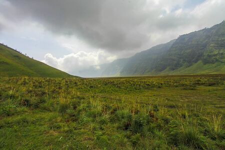 Green valley in Bromo National Park with dramatic cloud formationの写真素材