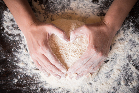 Female hands holding dough in heart shapeの写真素材