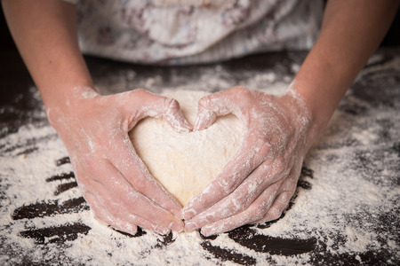 Cooking with love. Female hands holding dough in heart shapeの写真素材