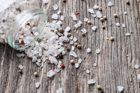 Whole peppercorns and crystal sea salt spilling from jarの写真素材