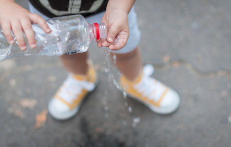 Little caucasian boy washing hands with a bottle of clear water outdoors. Hygiene concept.の写真素材