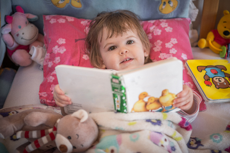 Little girl reads children's book in bed before sleepの写真素材