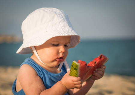 Caucasian baby girl on sandy beach eating watermelonの写真素材