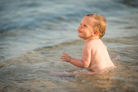 Happy adorable little girl sitting in water on sand beachの写真素材
