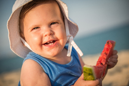 Caucasian baby girl on sandy beach eating watermelonの写真素材
