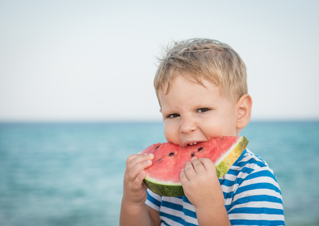 Caucasian boy eating watermelon on beachの写真素材