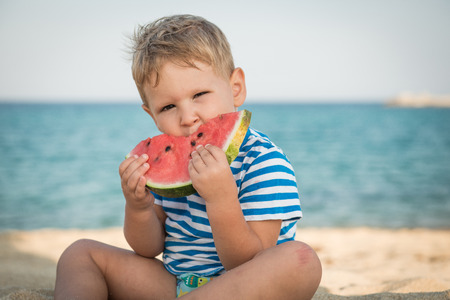 Caucasian boy eating watermelon on beachの写真素材