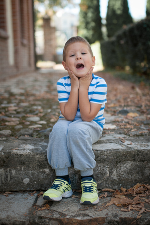 Little caucasian boy sitting at park and making grimaceの写真素材