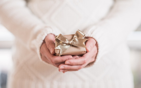 Female hands holding small gift with golden ribbonの写真素材