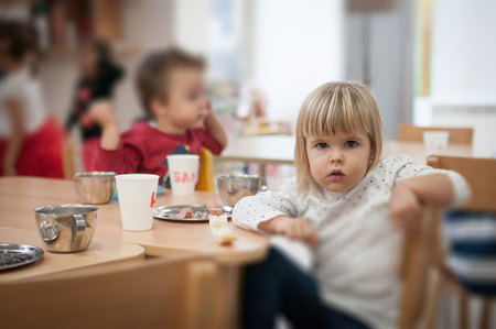 Little caucasian girl having breakfast in kindergarten, portrait looking at cameraの写真素材