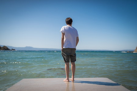 Boy standin alone on dock looking out to seaの写真素材
