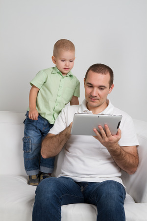 Dad and son watching the tablet sitting on the couchの写真素材
