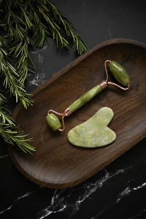 Rosemary jade facial massage roller on a wooden tray over black marble backgroundの写真素材