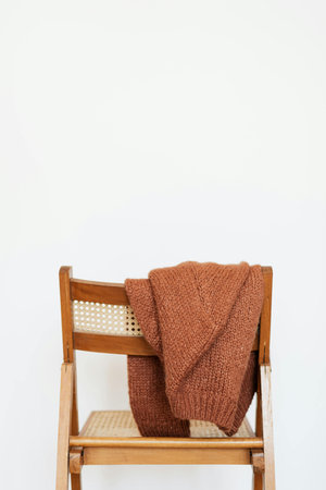Knitted woolen sweater on a wooden chair against a white wallの写真素材