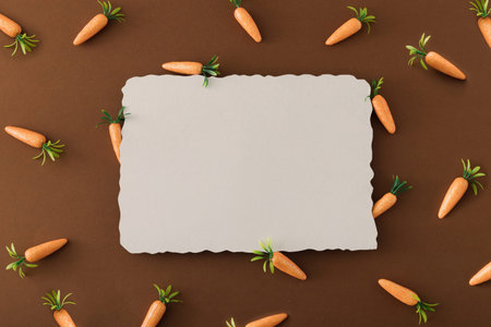 Easter pattern made with carrots and paper card note against a brown background.Creative Easter...
