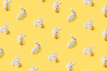 Pattern made with rabbits, Easter concept against  yellow background. The rabbit holds a golden Easter egg. Minimum flat lay.の写真素材