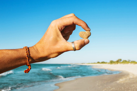Man holding heart stone in hand on sea beach backgroundの写真素材