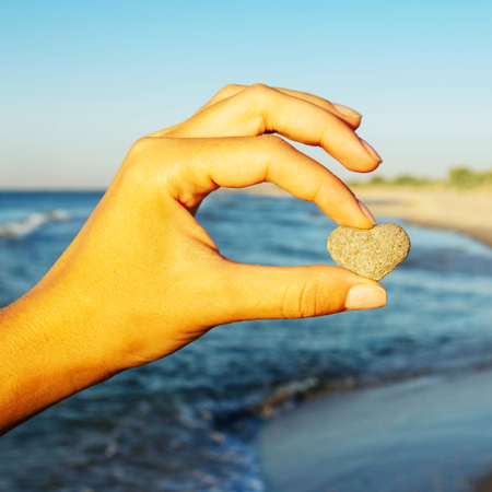 Woman holding heart stone in hand on sea beach backgroundの写真素材